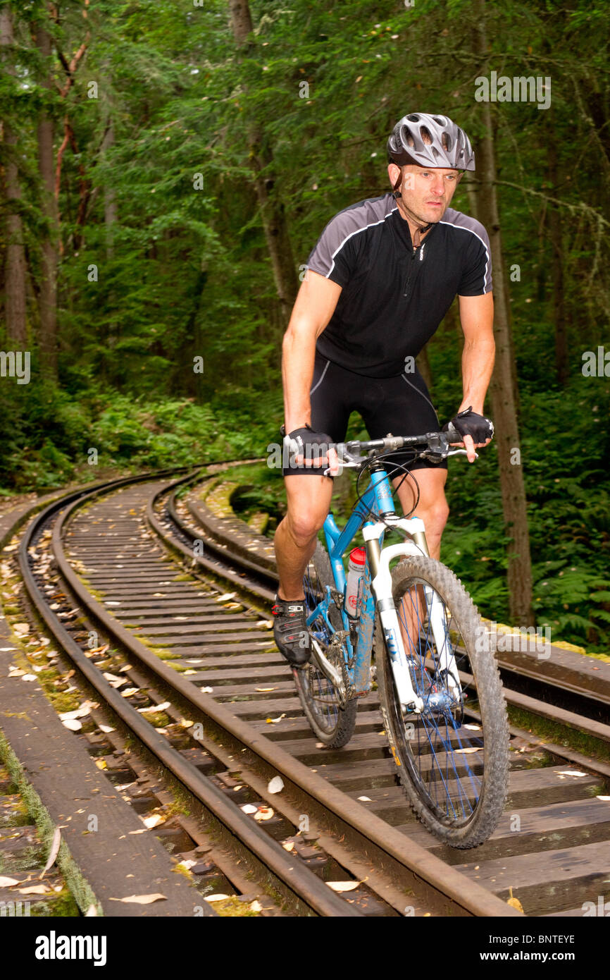 Male bike rider rides along railroad tracks in the woods Stock Photo