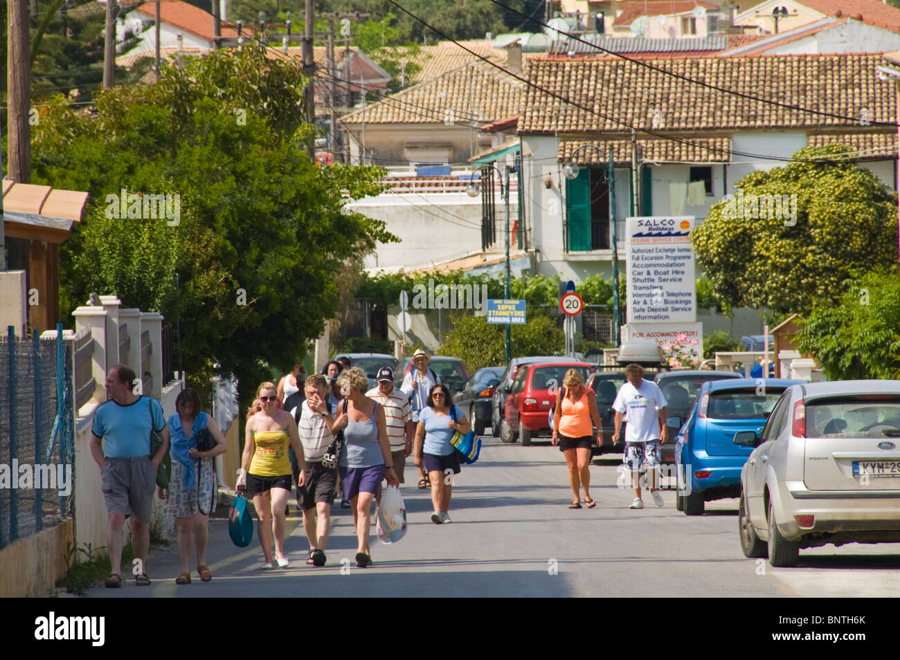Tourists walking in the street at Kassiopi on the Greek Mediterranean island of Corfu Greece GR Stock Photo