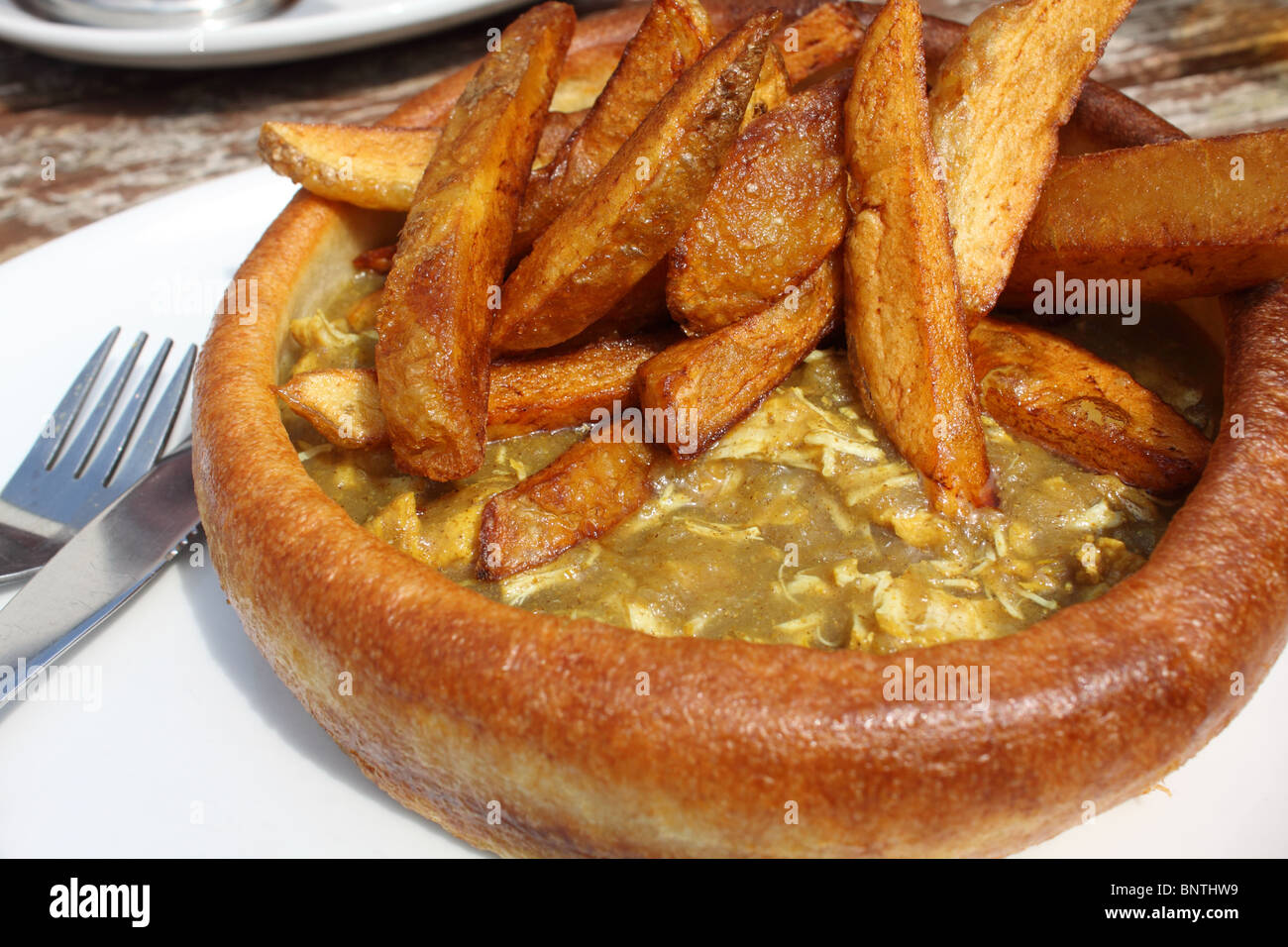 giant Yorkshire pudding, a traditional English meal, but with a filling of chicken curry, served with potato chips Stock Photo