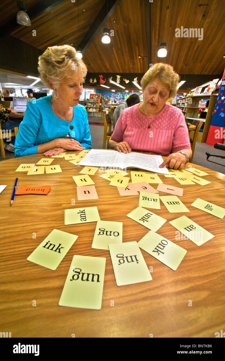 A volunteer reading instructor teaches reading to an elderly Hispanic woman at a public library