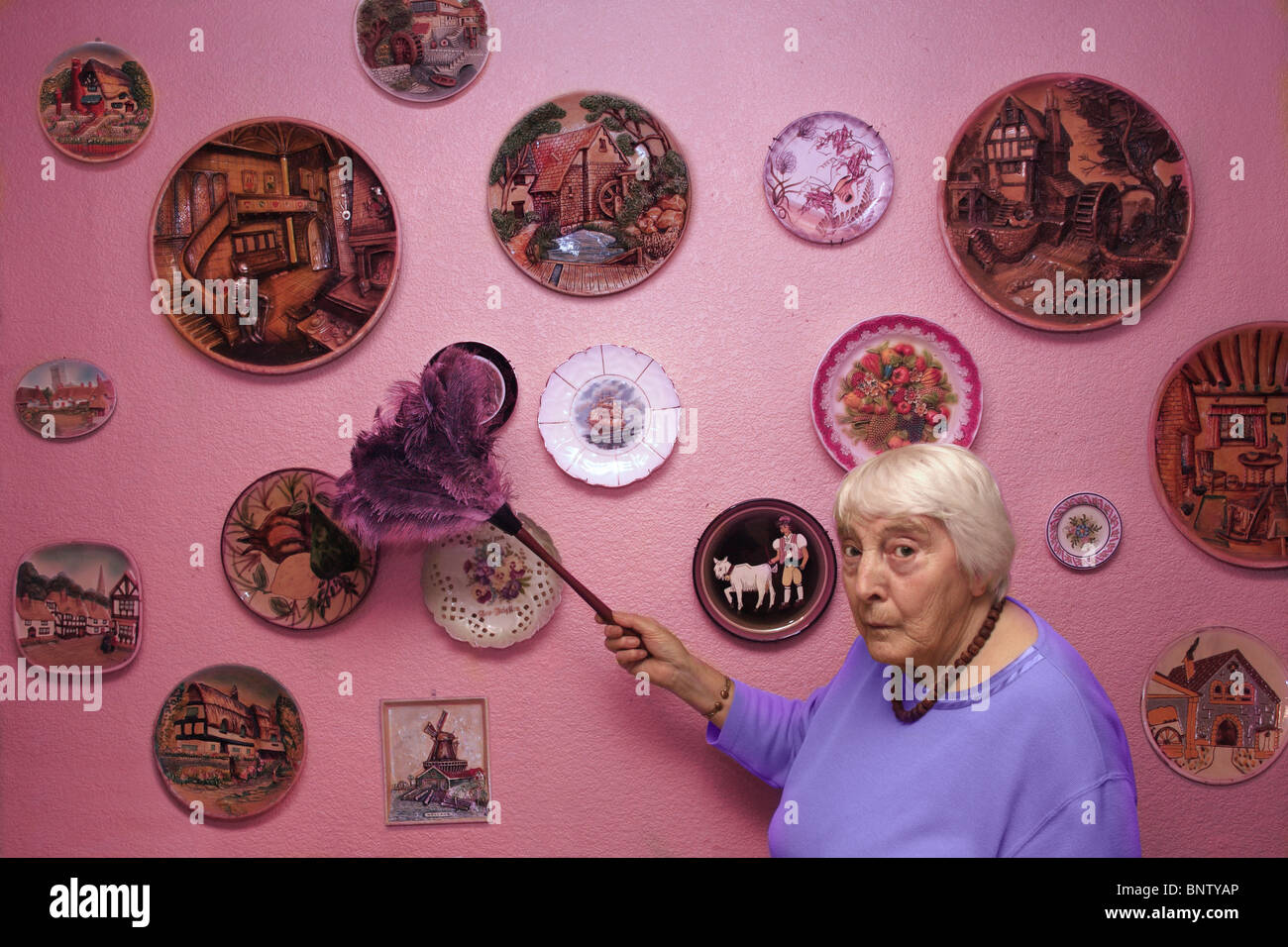 An old lady dusting her collection of plates. Stock Photo