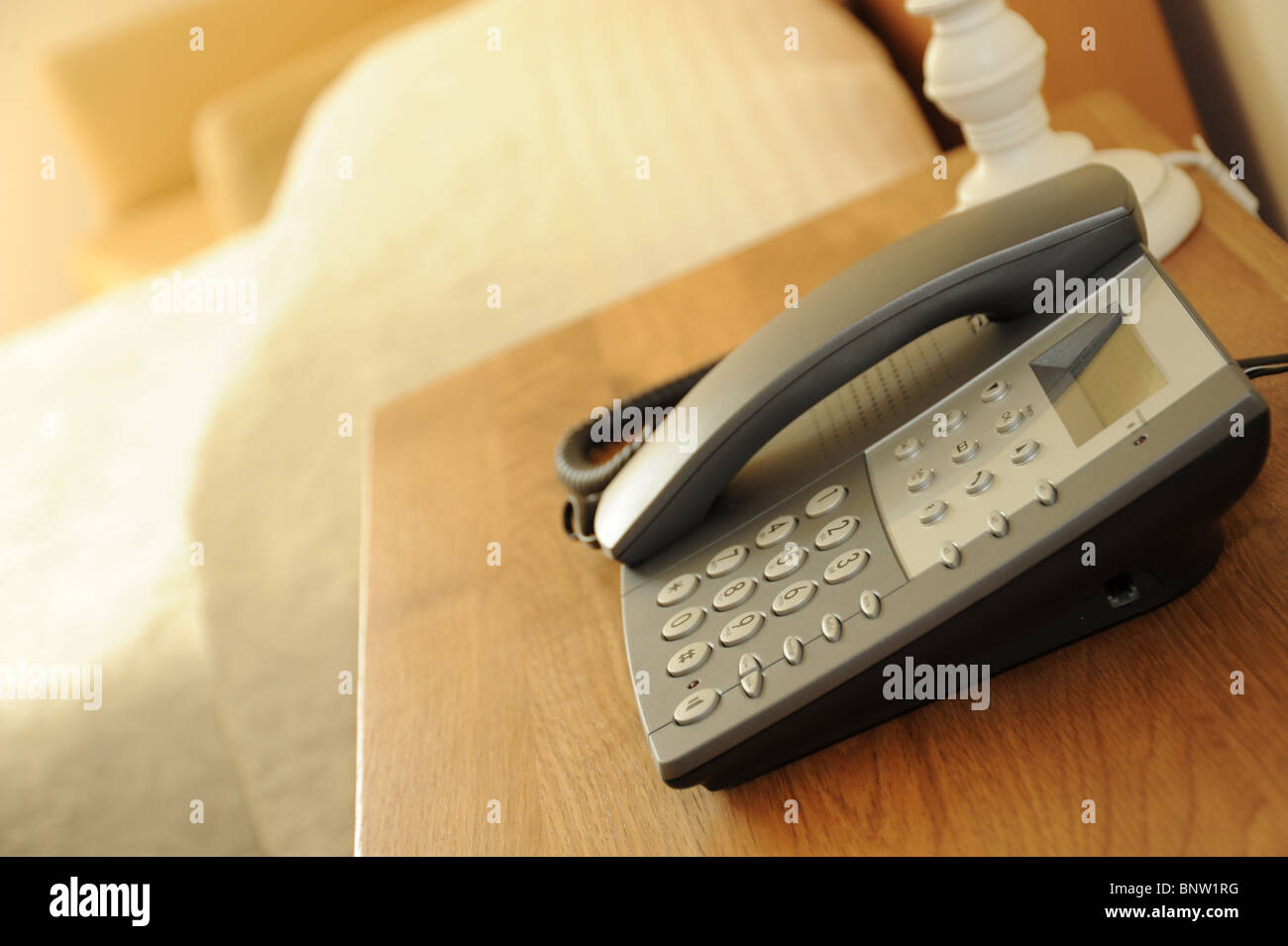 Telephone on a bedside table by a bed Stock Photo