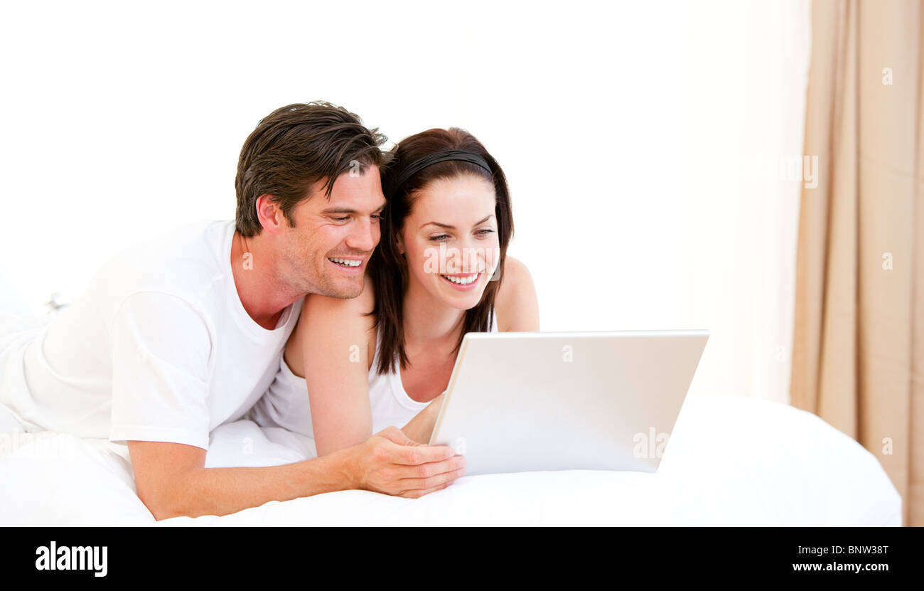 Cheerful couple using a computer lying on their bed Stock Photo - Alamy