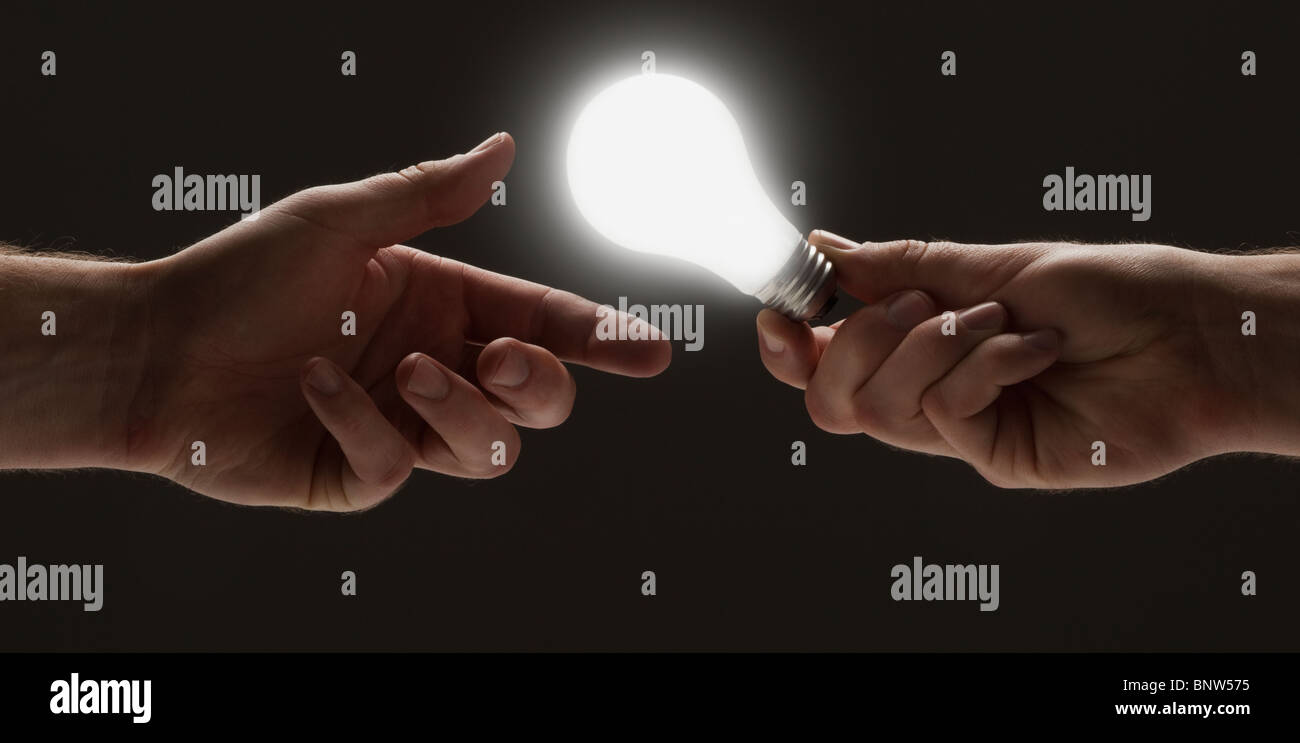 Hand passing a light bulb to another hand Stock Photo