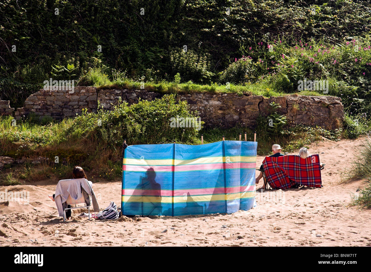 Holidaymakers on the beach behind a windbreak, Benllech, Anglesey, North Wales, UK Stock Photo