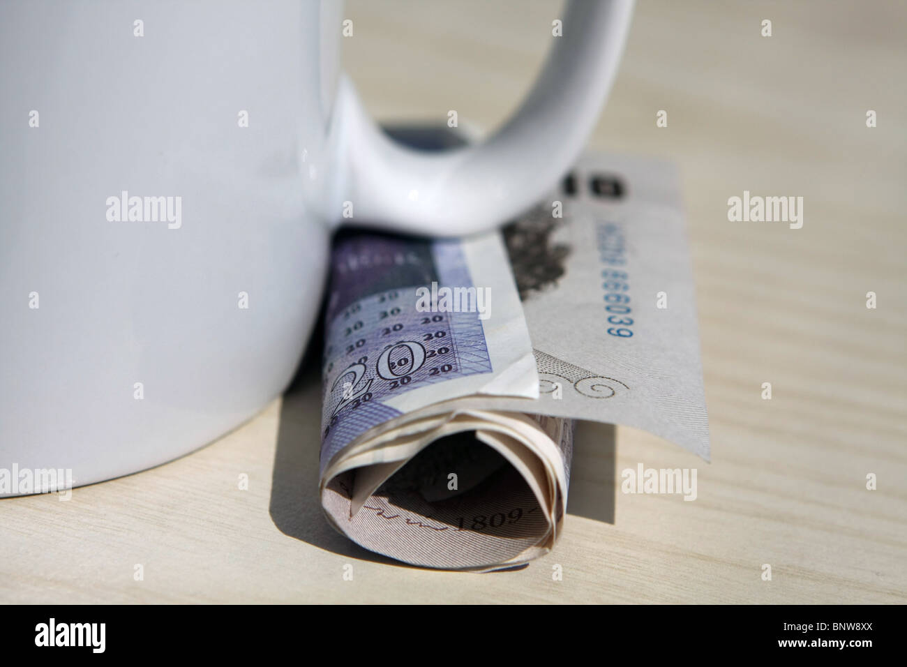 folded £20 and £10 notes under the handle of a white mug Stock Photo