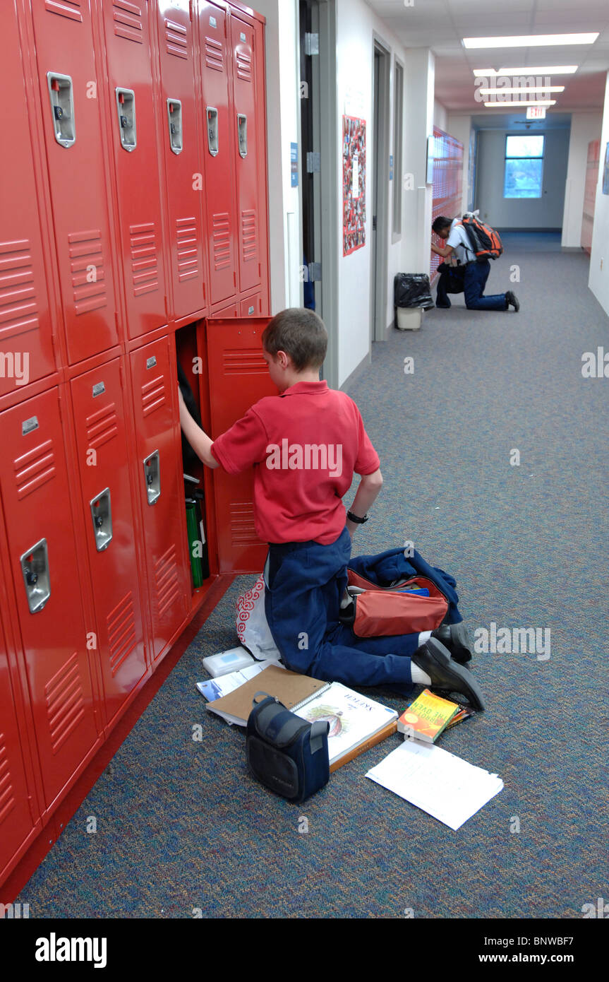 Anglo male middle school student takes out books and organizes his locker in hallway of school in Texas Stock Photo