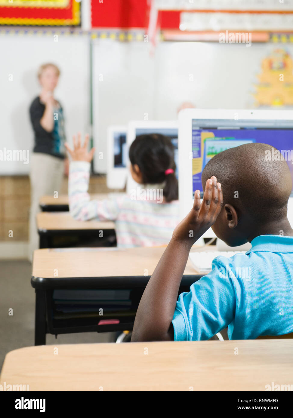 Elementary school students raising their hands in classroom Stock Photo