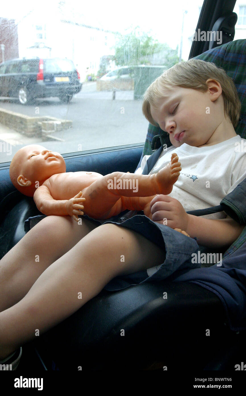 Young boy asleep in car seat with doll on his lap. Stock Photo