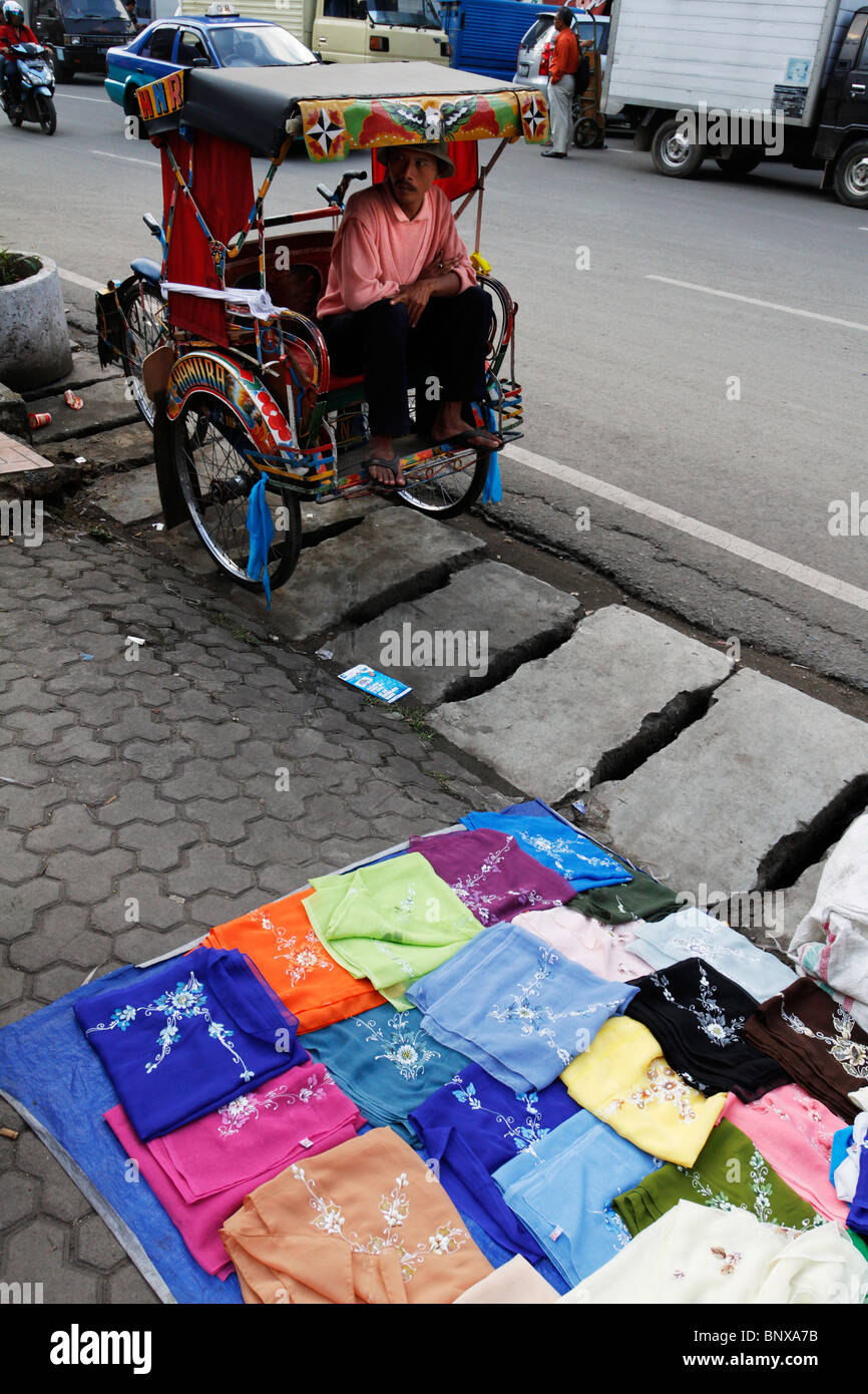 Trishaw and colourful clothes for sale on the sidewalk in Bandung