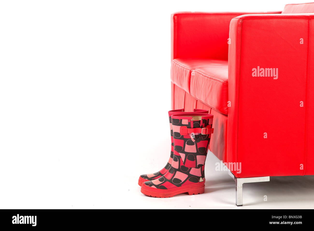 Pair of Stylish Wellingtons in front of a Red Couch on a White Isolated Background Stock Photo