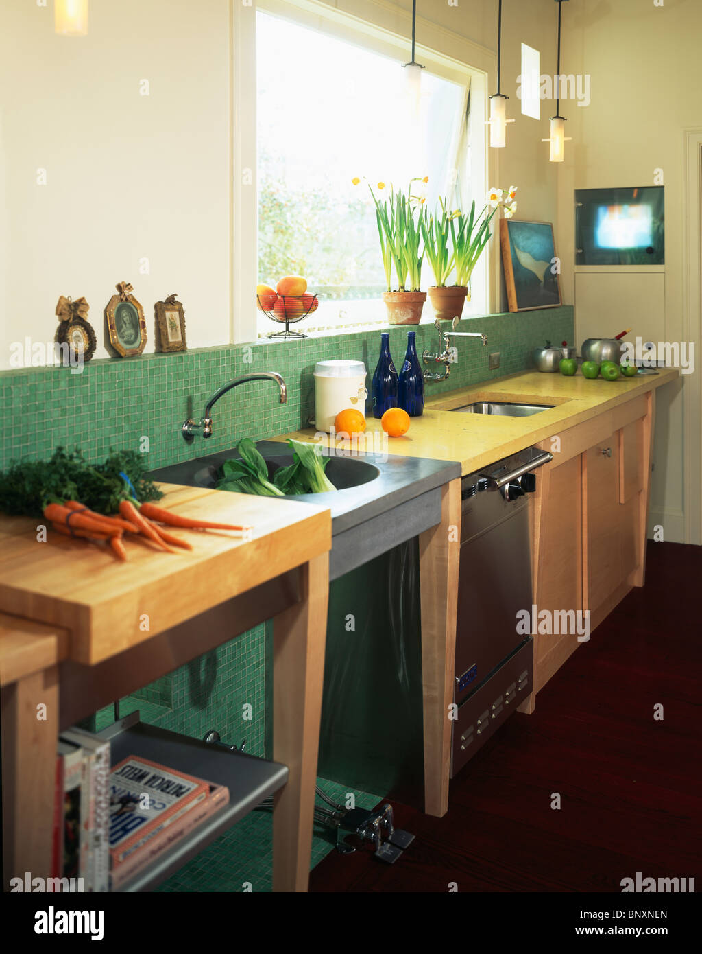 Bunch of carrots on freestanding unit beside steel sink in modern galley  kitchen with green tiled splash-back Stock Photo - Alamy