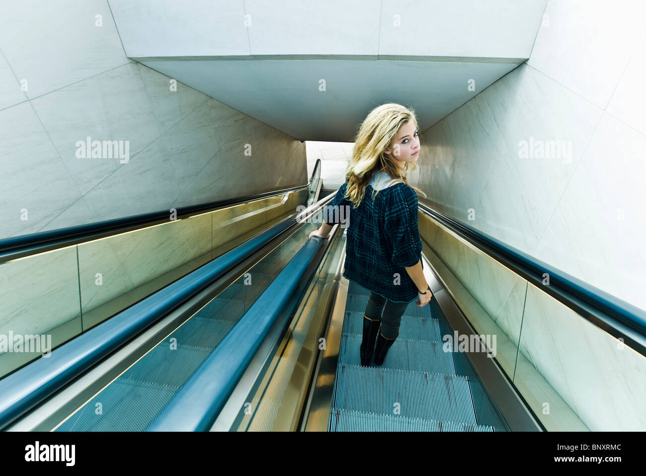 Teen girl riding escalator, looking over shoulder at camera Stock Photo