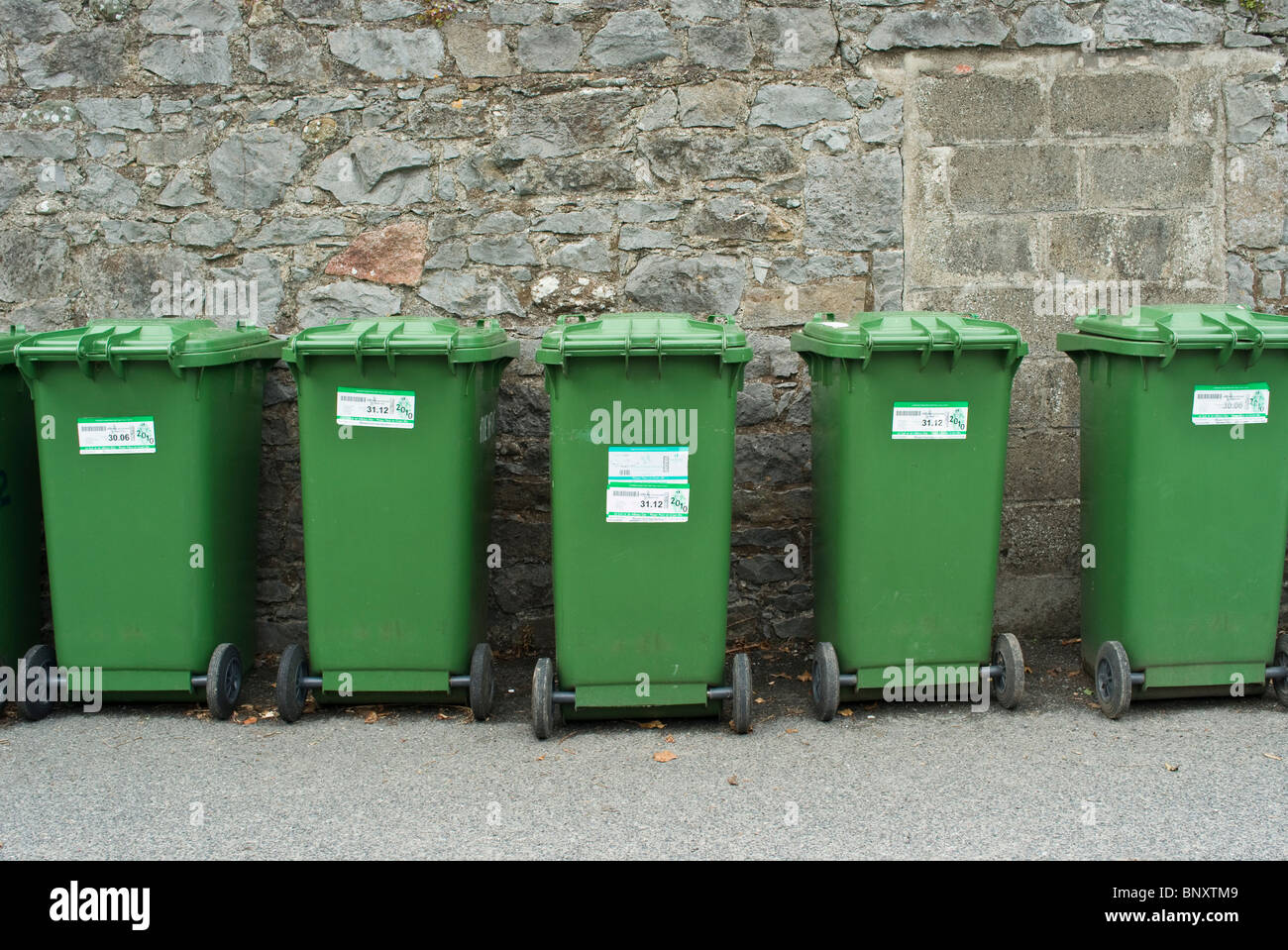 A lin of recycling green wheelie bins against a wall Stock Photo