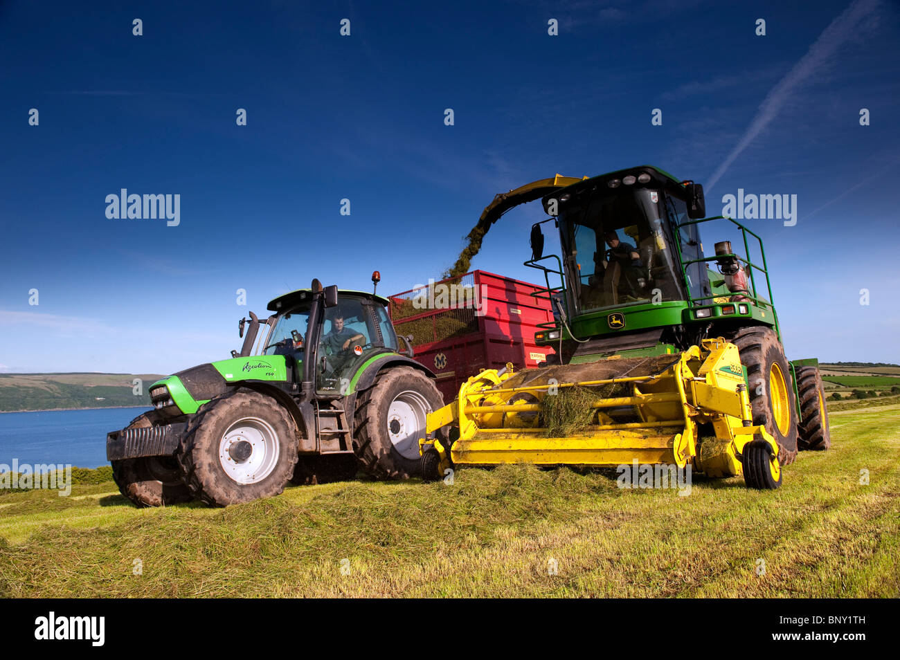 Silage making on the coast of Loch Ryan near Stranraer with Deutz Fahr tractor and John Deere chopper Stock Photo