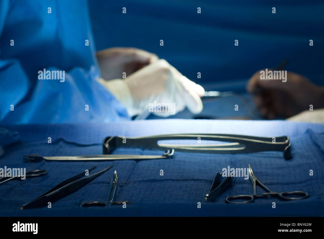 Surgical instruments arrayed on tray, surgeons operating in background ...