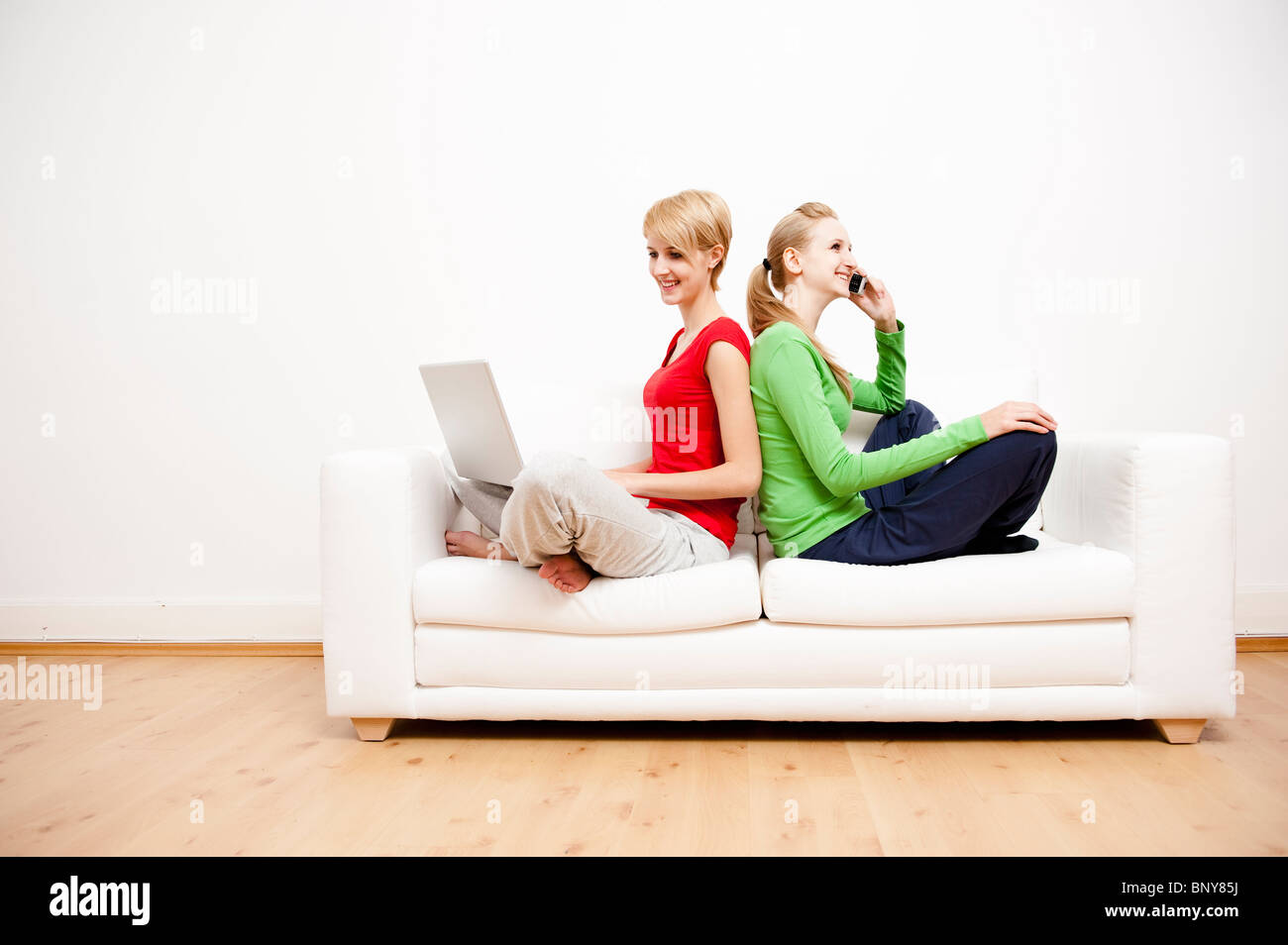 Two women using laptop and phone on sofa Stock Photo - Alamy