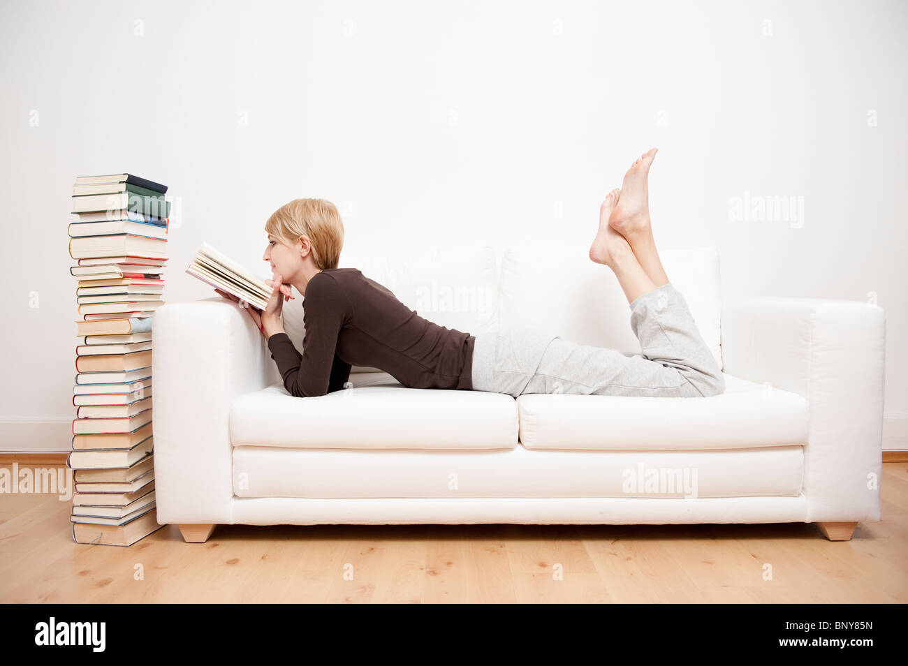 Woman reading a book on sofa Stock Photo Alamy