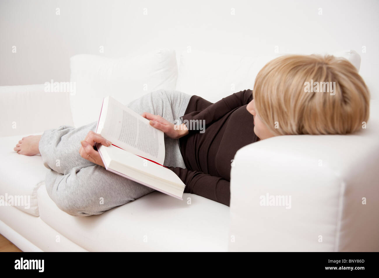Woman reading a book on sofa Stock Photo Alamy