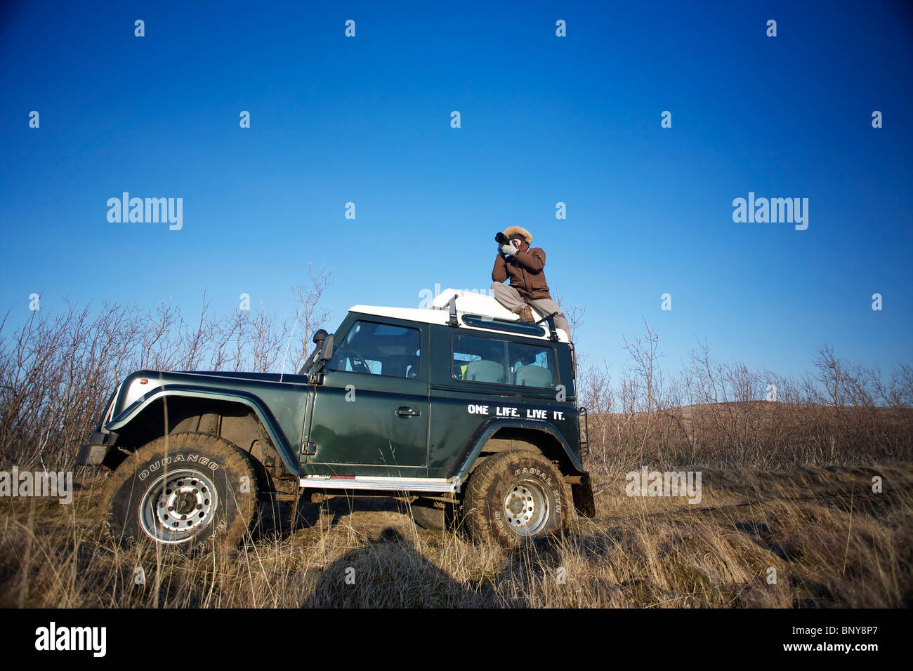 A photographer takes a shot on top of a Land Rover Defender 90 - 300TDI in Iceland Stock Photo