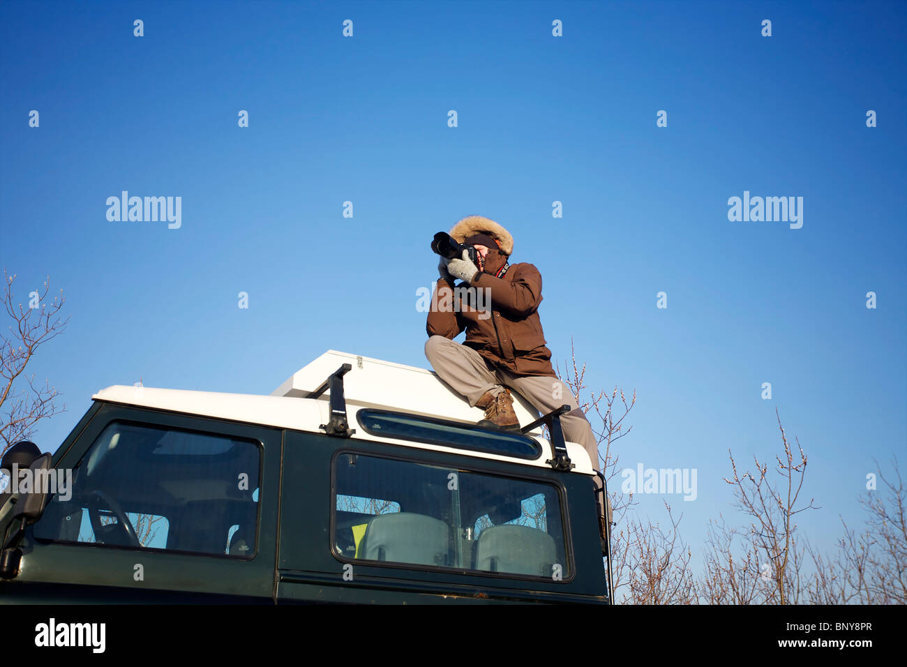 A photographer takes a shot on top of a Land Rover Defender 90 - 300TDI in Iceland Stock Photo