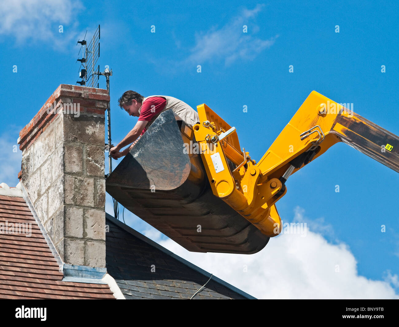 Television aerial being fitted to chimney by man standing (no safety equipment) in JCB Telescopic Handler bucket - France. Stock Photo