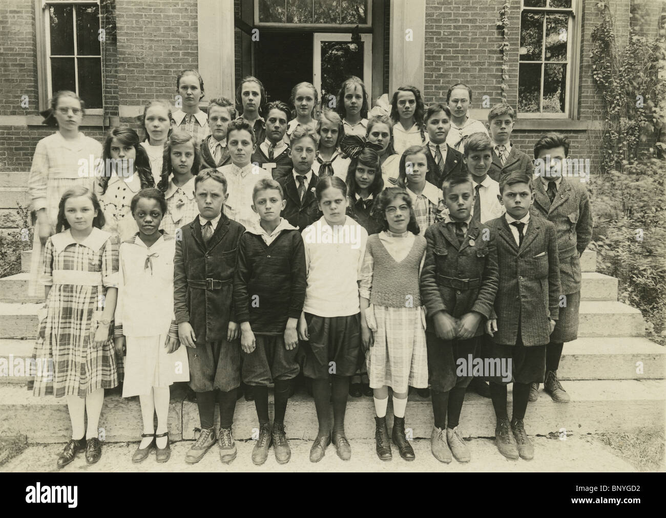 Circa 1900 school photo, showing a group of caucasian 9-11 years old with an African American girl. Stock Photo