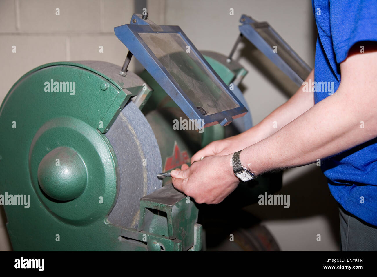 Engineer sharpening or grinding a drill on abrasive grinding wheel with