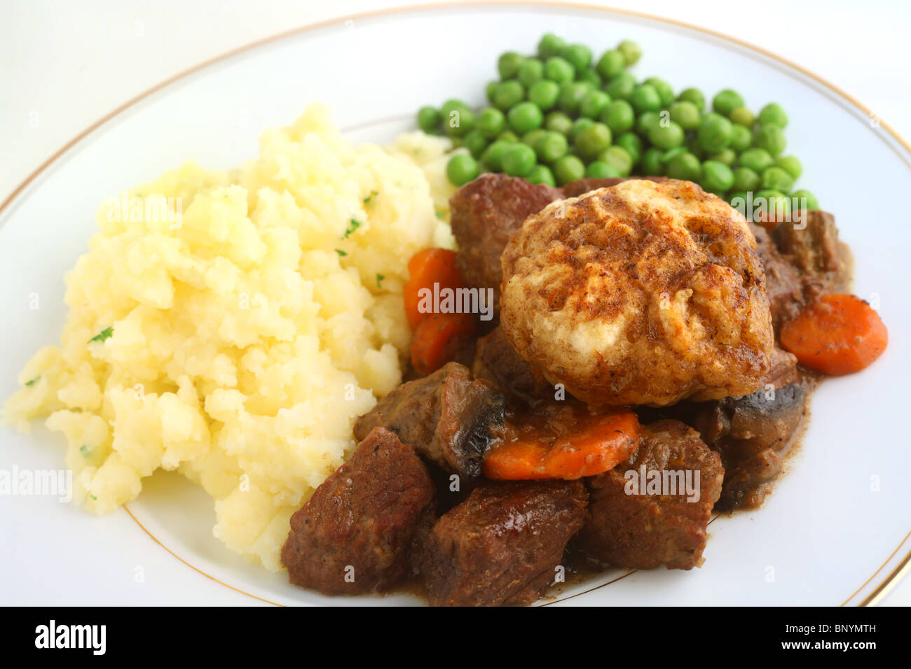 Traditional British beef stew topped with dumplings and served with parsley mashed potatoes and peas. Stock Photo