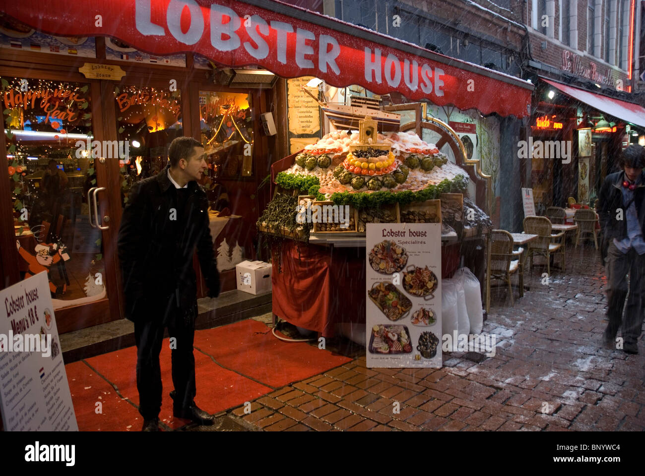 Waiter looking for patrons on Rue des Bouchers restaurants street in Brussels under snow Stock Photo