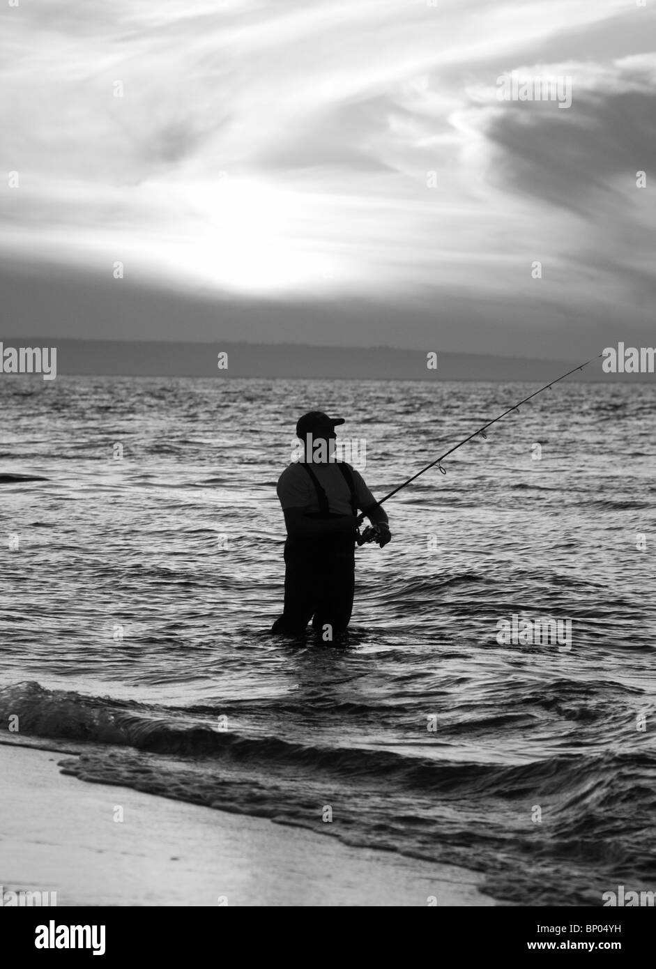 Black and White Image of Man fly-fishing in the ocean at sunset. Stock Photo