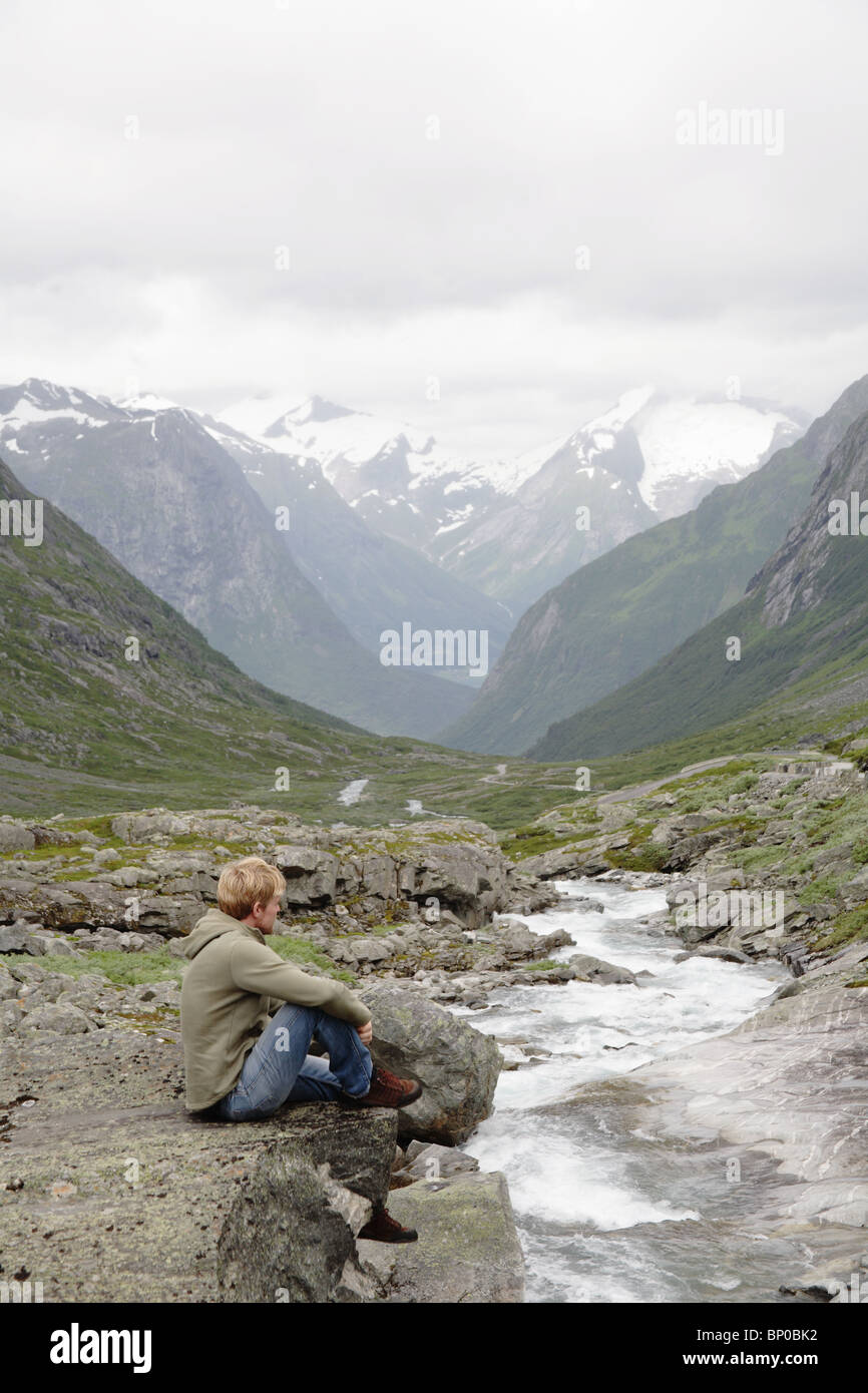 Man sitting by stream and mountains Stock Photo