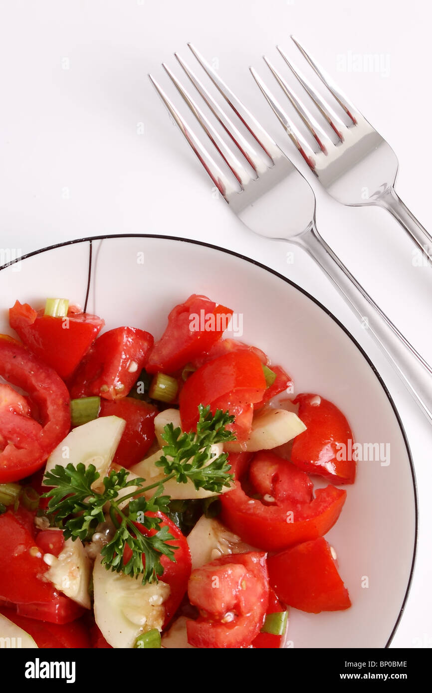 Red tomato and parsley salad isolated on white with silver forks Stock Photo