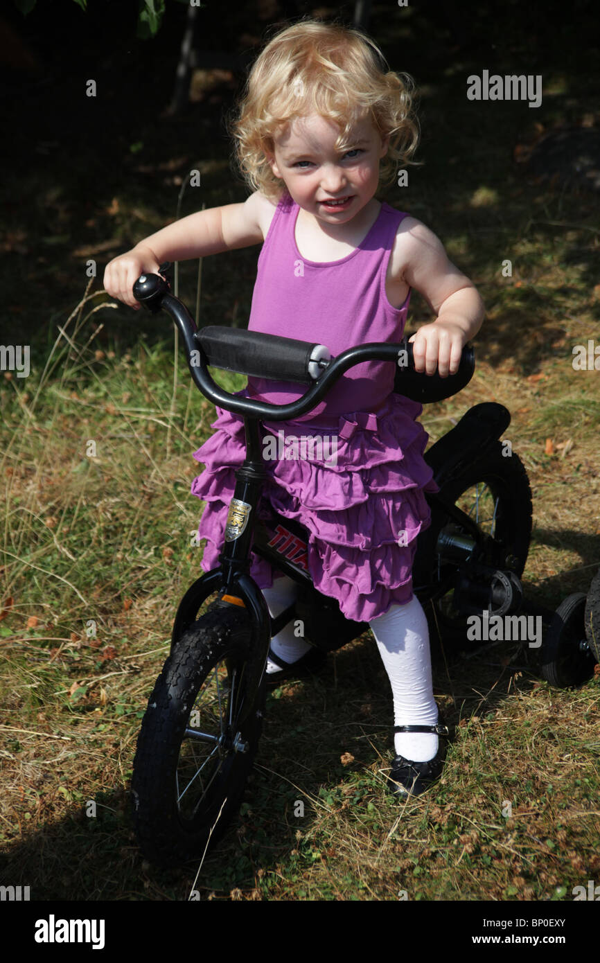 Little girl toddler in party clothes dressed up sitting on a bicycle MODEL RELEASED Stock Photo