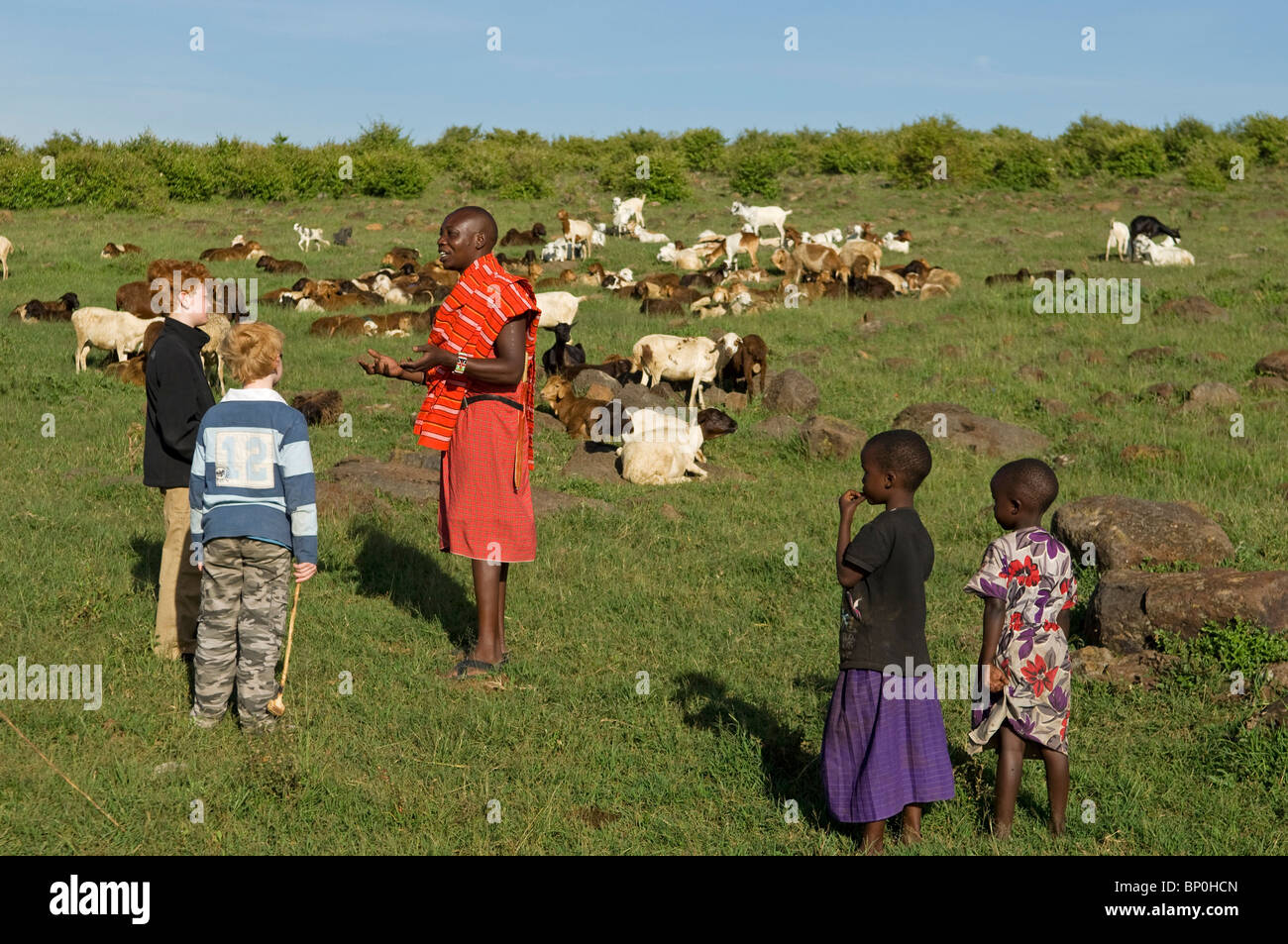 Kenya, Masai Mara. Safari guide, Salaash Ole Morompi, explains life in a Maasai manyatta to boys on safari. (MR) Stock Photo