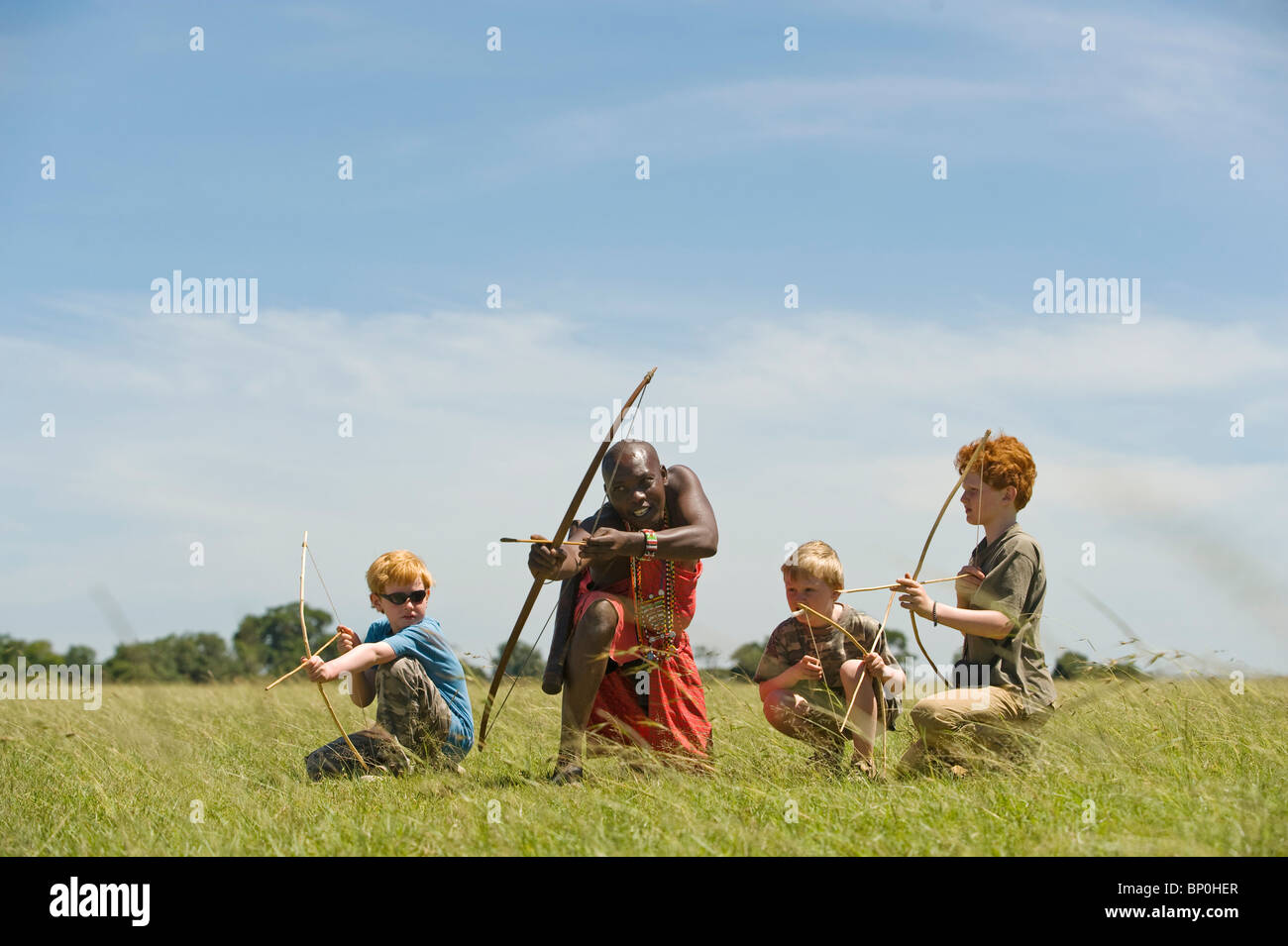 Kenya, Masai Mara. Safari guide, Salaash Ole Morompi, teaches children archery Maasai style. (MR) Stock Photo