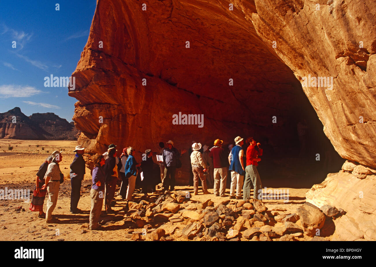 Libya, Fezzan, Jebel Akakus. Tourists gather at the mouth of Uan Amil, one of Wadi Teshuinat's caves. Stock Photo