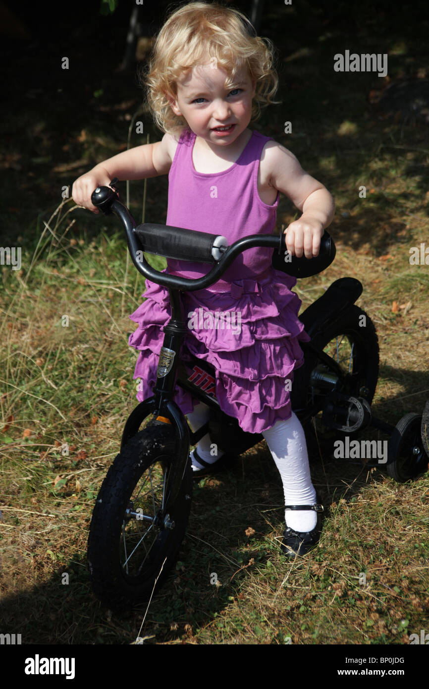 Little girl toddler in party clothes dressed up sitting on a bicycle MODEL RELEASED Stock Photo