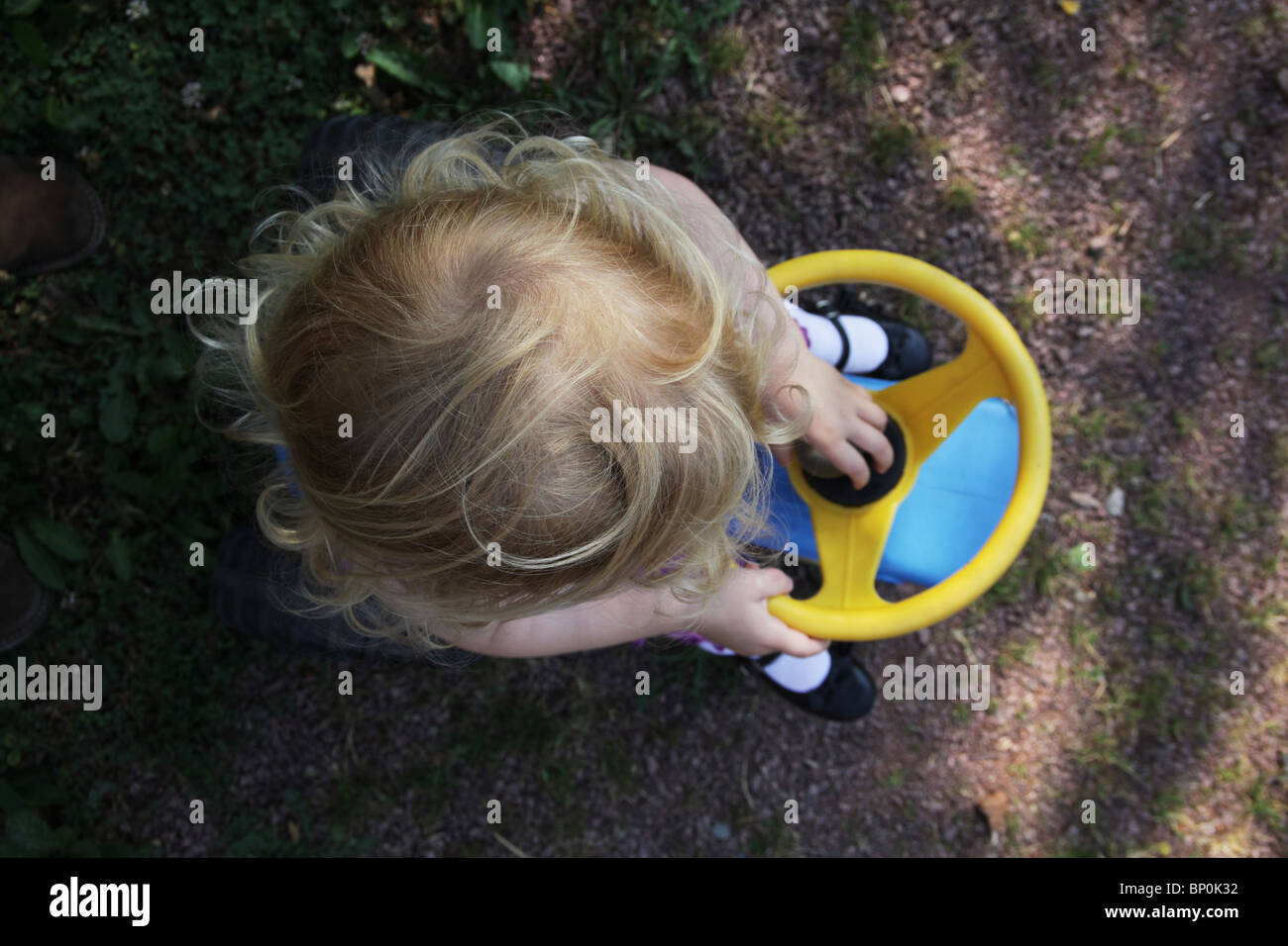 Little girl toddler in sitting on a plastic toy tractor holding the steering wheel aerial view MODEL RELEASED Stock Photo