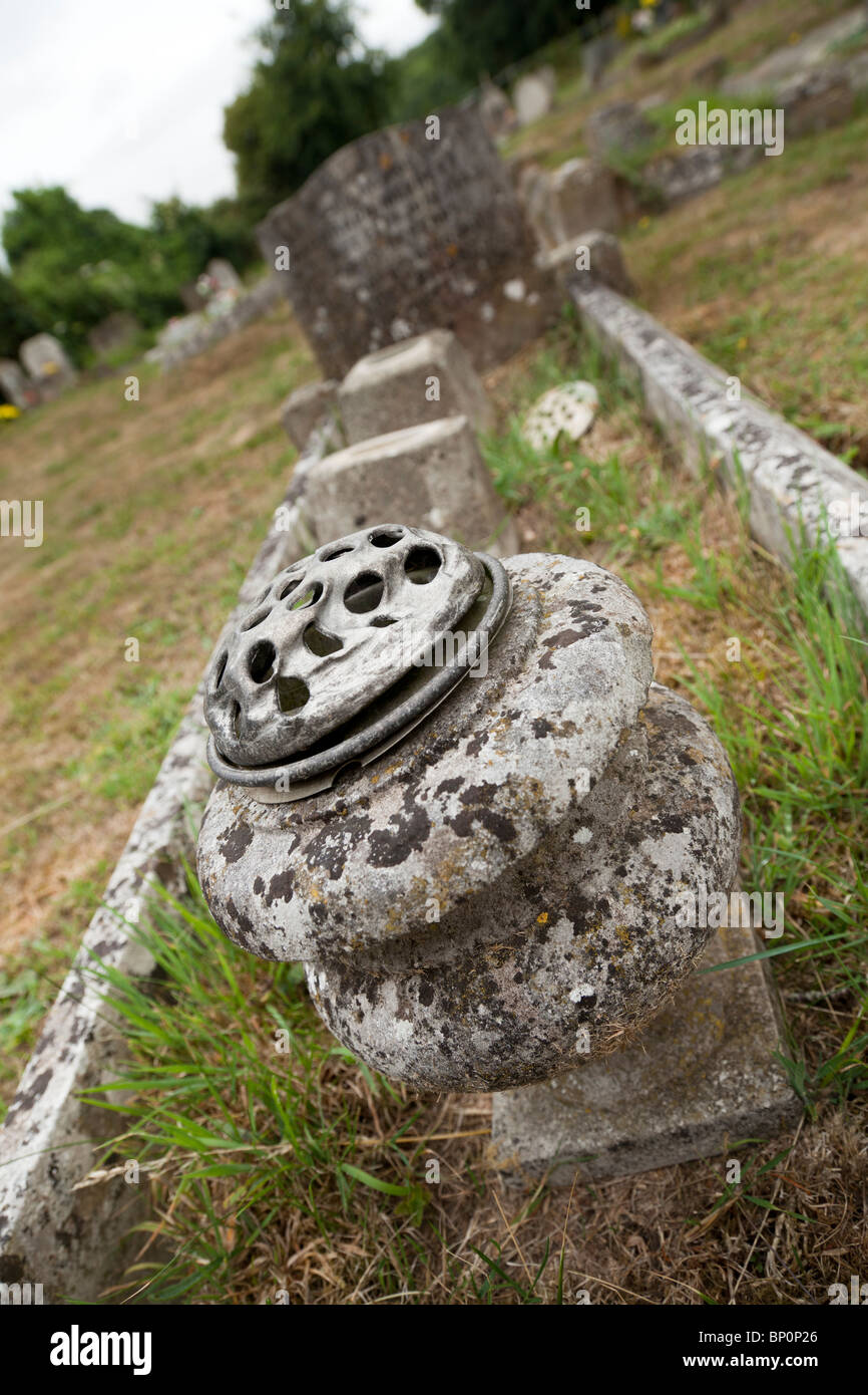 Old weathered stone flower pot on an unkempt grave in an english village churchyard Stock Photo