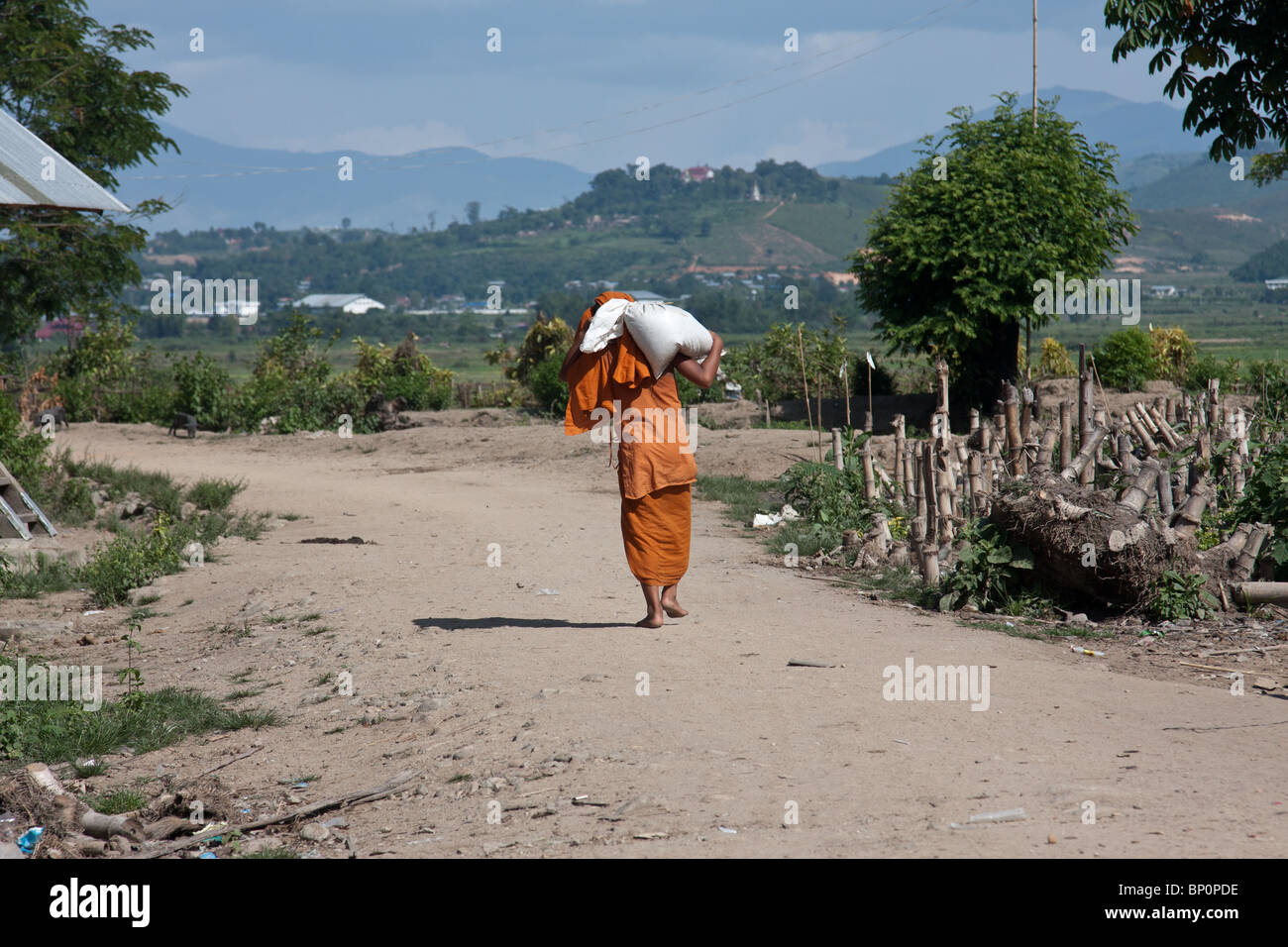 monk carrying a heavy bag over his shoulder walking barefoot down a