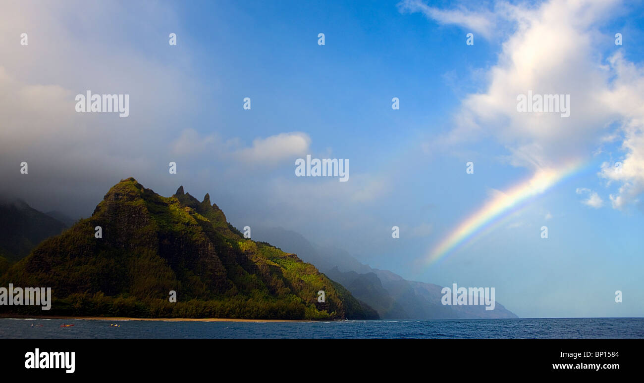 A vivid early morning rainbow greets kayackers near Kee Beach and the start of the Na Pali coastline, north shore, Kauai, Hawaii Stock Photo