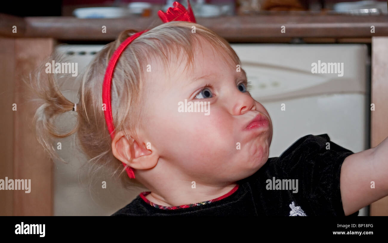 This toddler girl in pigtails and red bows in her blond hair, has over stuffed her mouth with food and is struggling to eat it. Stock Photo