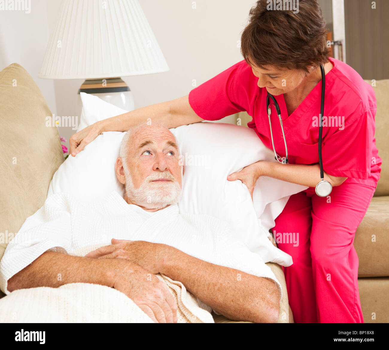 Home health nurse fluffs an elderly patient's pillow.  Stock Photo