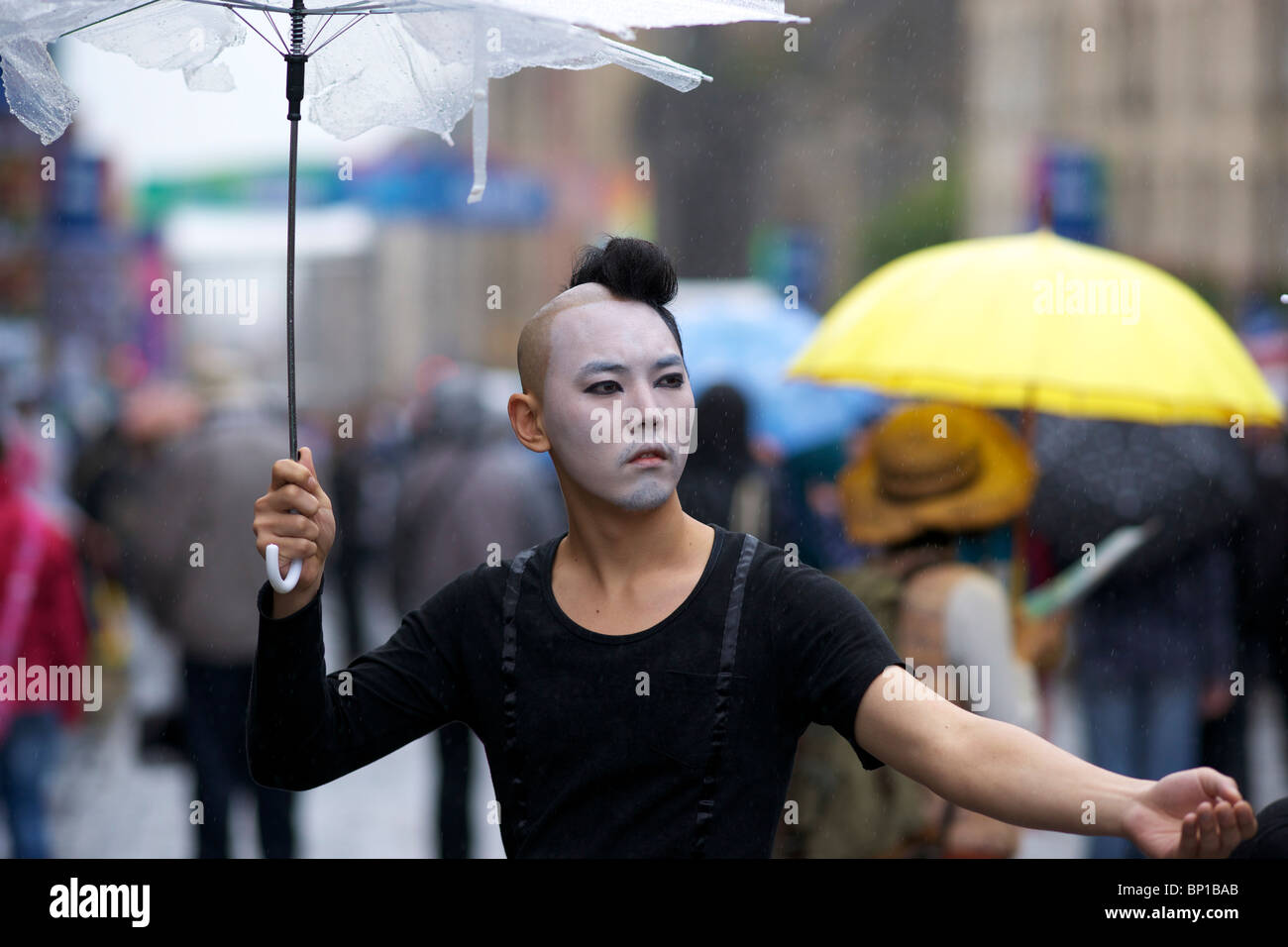 Male Performer in High Street Edinburgh holding umbrella during the rain. Holds hand out. Stock Photo