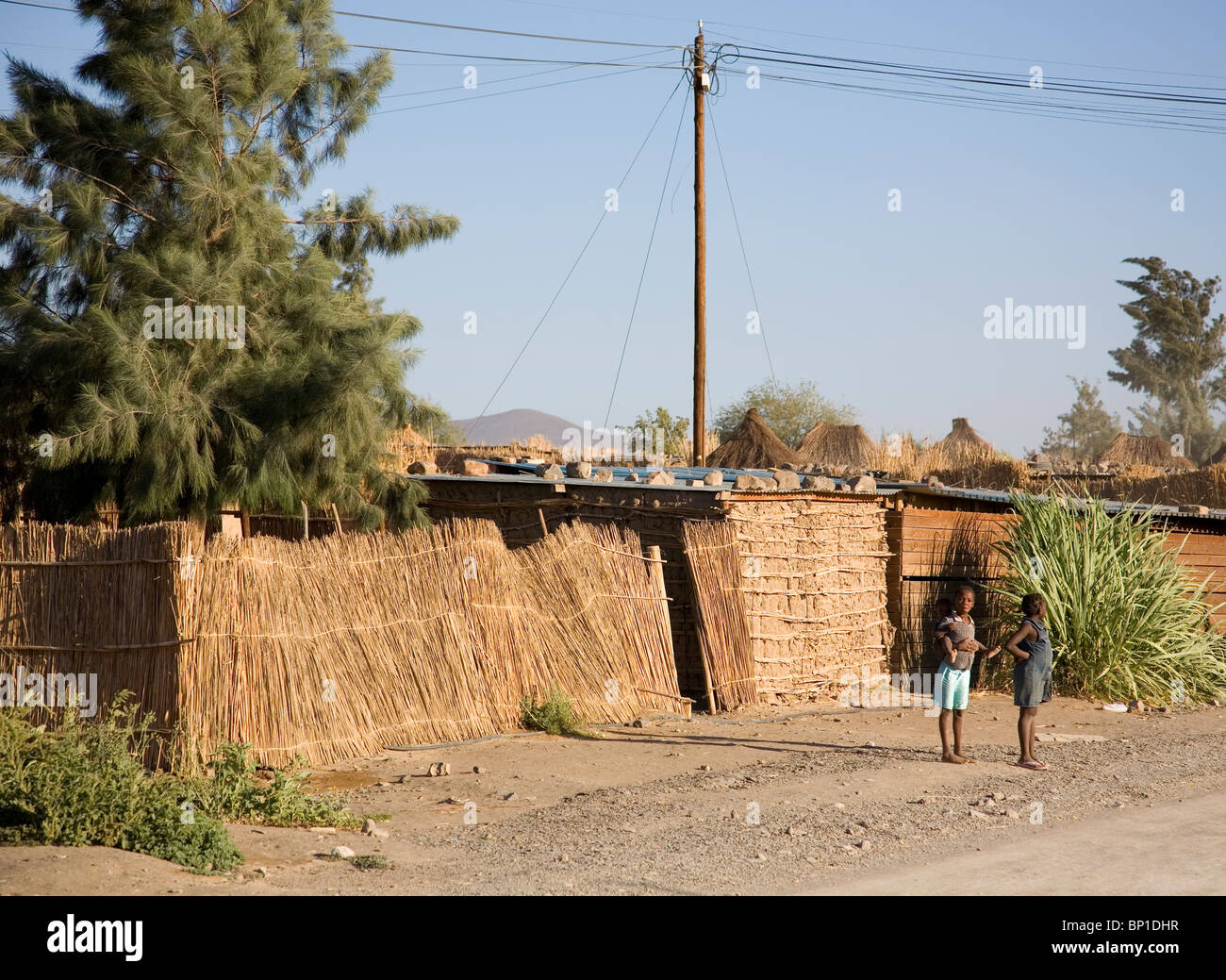 Two girls, one with baby on back, standing by roadside in Aussenkehr Village - namibia Stock Photo
