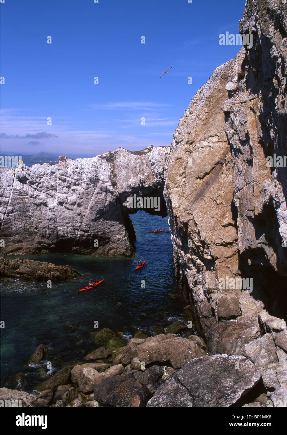 Sea kayakers paddling beneath Bwa Gwyn, natural sea rock arch near Rhoscolyn Ynys Gybi Anglesey North Wales UK Stock Photo