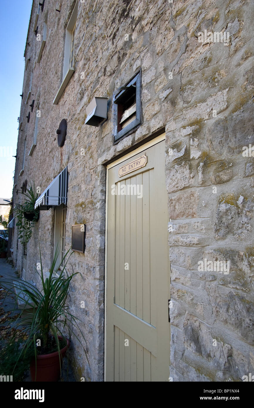 The back door with a sign that reads 'No Entry' of an old stone building, with awnings over the windows. Stock Photo