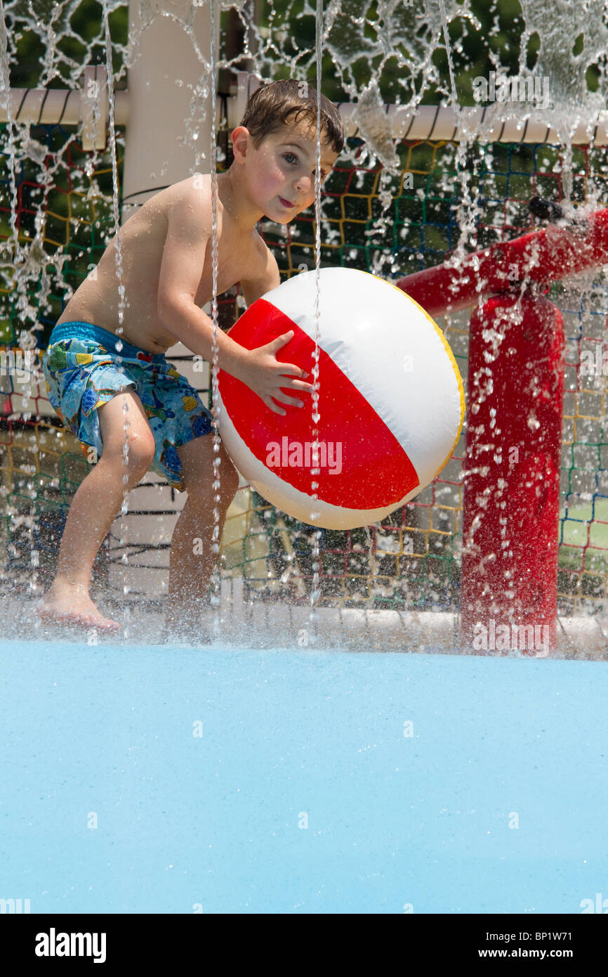 Four year old boy playing with beach ball at an elaborate swimming pool
