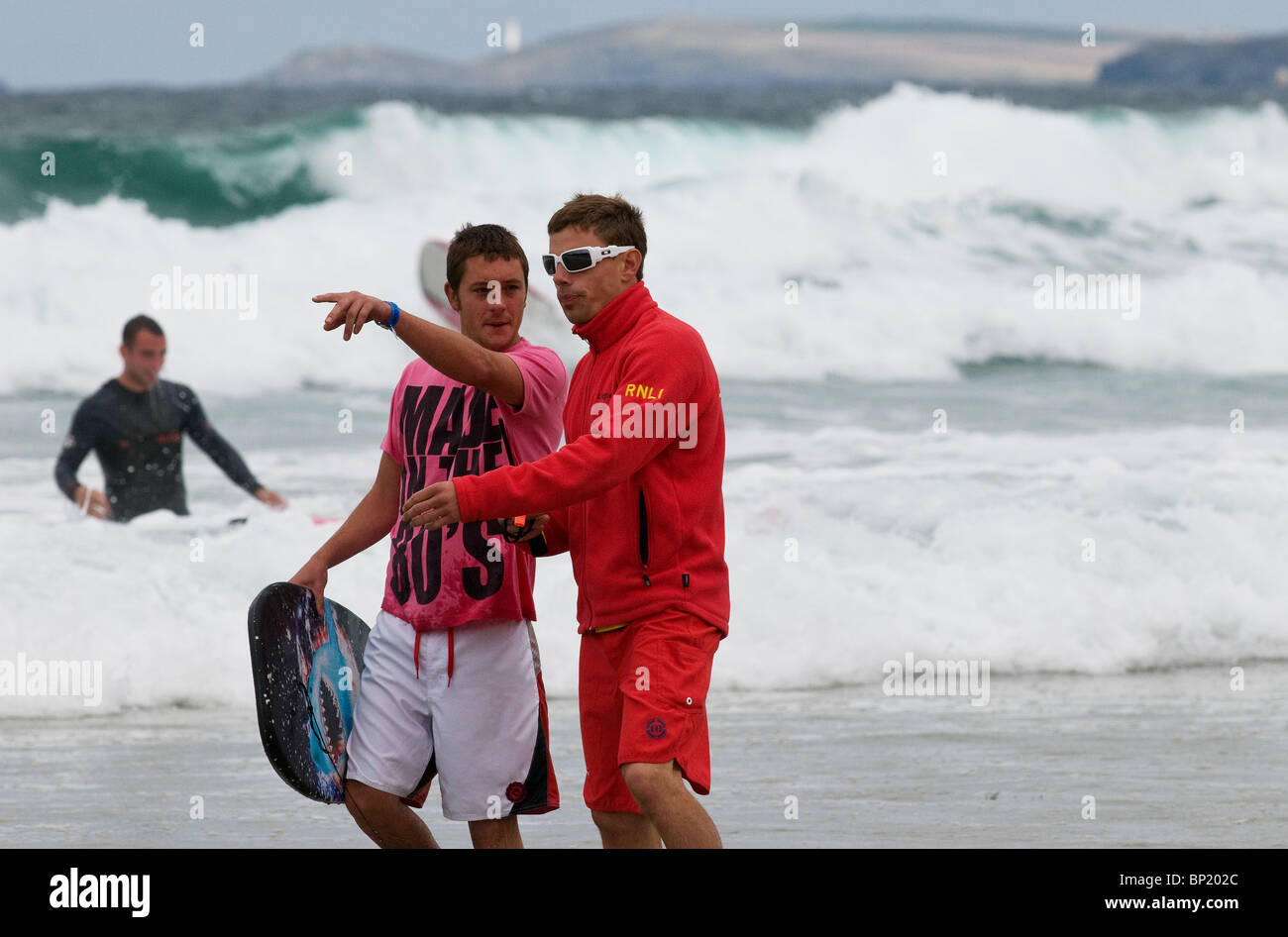 A RNLI lifeguard advising a holidaymaker on the beach at Newquay in Cornwall. Stock Photo